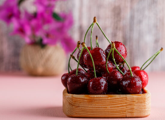 Cherries with flower pot in a wooden plate on pink and grungy background, side view.