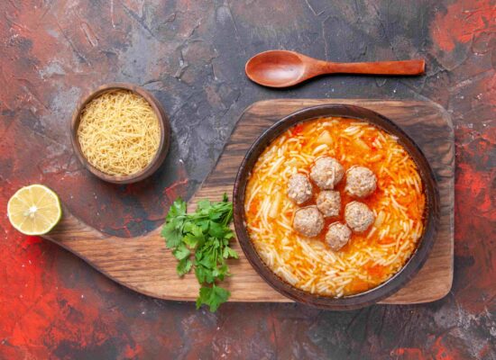 top-view-tasty-chicken-soup-with-noodles-wooden-cutting-board-uncooked-pastas-small-bowl-greens-dark-background